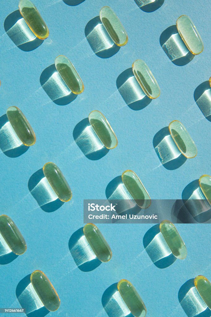 Fish oil pills pattern on a pastel blue background. Flat lay creative design. Omega D3 vitamin. Capsule - Medicine Stock Photo
