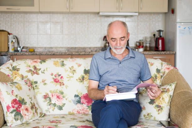 istock Handsome man sitting on sofa at home with books and doing homework 1412662127