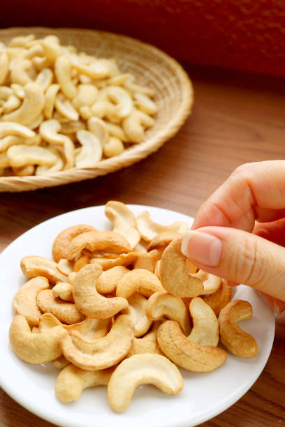 Woman's Hand Picking a Roasted Cashew Nut Kernel from Snack Saucer