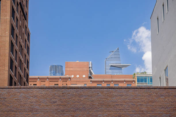 New York, NY, USA - June 24, 2022: Modern high rise buildings at Hudson Yards with older brick building in front seen from the High Line Park on a clear summer day