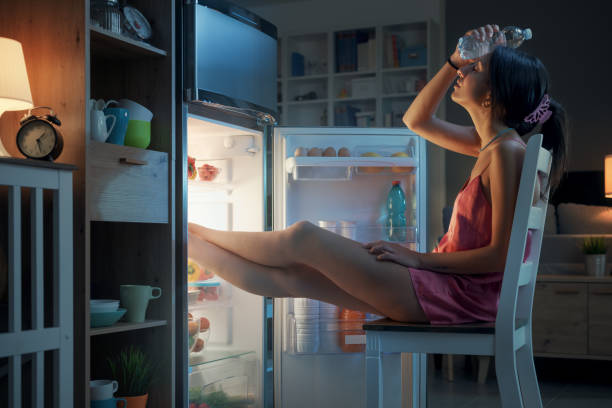 Woman cooling herself in front of the open fridge Woman suffering from the heat in summer, she is resting with her feet in the fridge and holding a water bottle sweat stock pictures, royalty-free photos & images