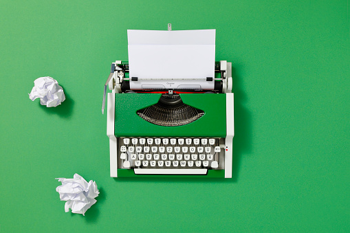 Green 70s typewriter with crumpled paper and a blank page on green backround