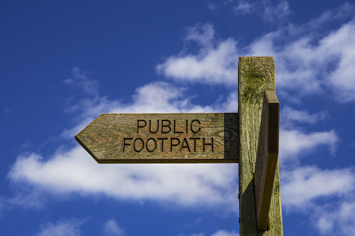 Wooden Public Footpath Sign isolated against Blue Sky with white clouds