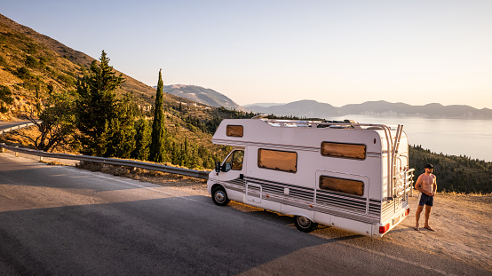 A man stands next to his motorhome parked at a viewpoint and enjoys the view of the sea