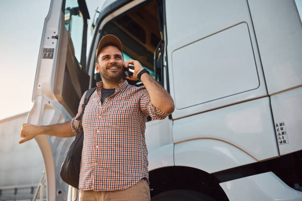 Happy truck driver communicating on cell phone while getting out of driver's cabin. stock photo