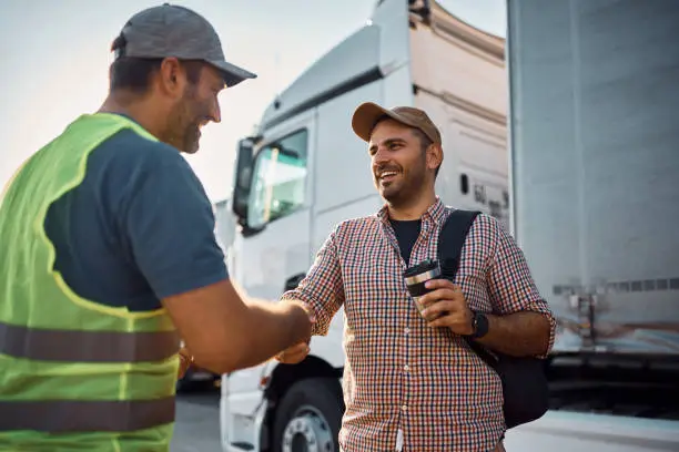 Photo of Happy truck driver and freight transportation manager greeting on parking lot.