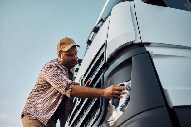 Below view of truck driver wiping headlights before the ride. Low angle view of young driver cleaning truck headlights on parking lot. Transport and Logistic Cleaning stock pictures, royalty-free photos & images
