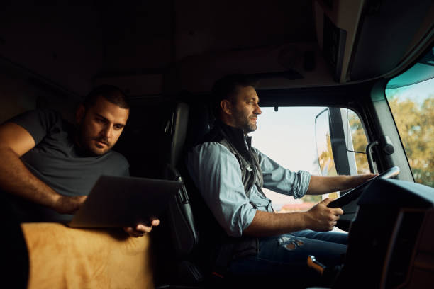 istock Professional driver driving truck while his colleague is using laptop in a cabin. 1412676372