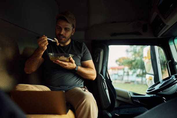 istock Truck driver eating lunch while using laptop in a cabin. 1412676664