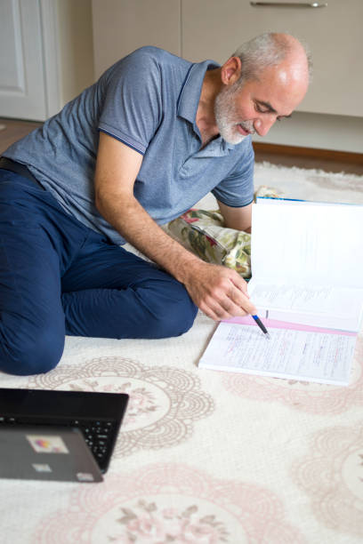 istock Handsome man sitting on carpet at home with books and doing homework 1412676780