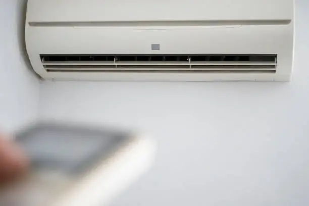 Photo of An unrecognizable person holding the remote control in front of the air conditioner at home