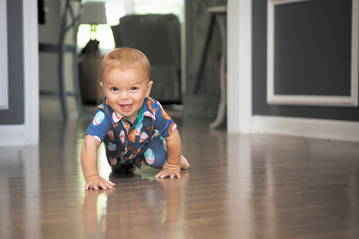 An 11 month old baby boysmiling as he crawls on the floor.