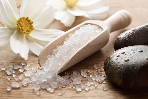 Wooden spoon with sea salt flowers and stones on wooden table - spa and wellness concept