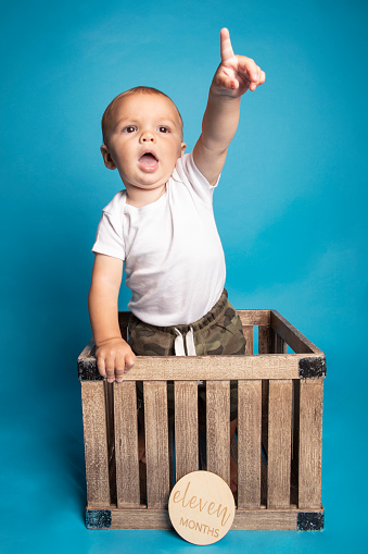 An 11 month old baby boy standing in a crate pointing his finger.