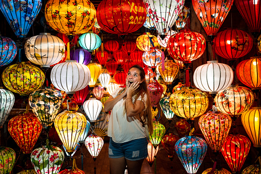 Young tourist surrounded by beautiful paper lanterns in Hoi An, Vietnam. Tourist dazzled by beautiful paper lanterns in Hoi An. Surprised woman. Surprised woman surrounded by paper lanterns in Hoi An, Vietnam