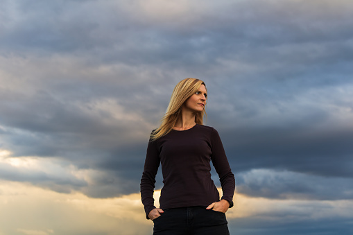 Portrait young blonde smiling caucasian woman. Hero pose with dramatic sky