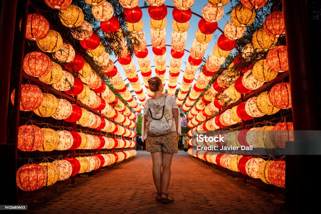 Tourist walking through beautiful arch of lights in Hoi An, Vietnam. Tourist walking through beautiful arch of lights in Hoi An, Vietnam. Tourist going through archway full of paper lanterns. Beautiful arch of paper lanterns in Vietnam. Lamp lit. Paperlamps. copy-space Vietnam Stock Photo