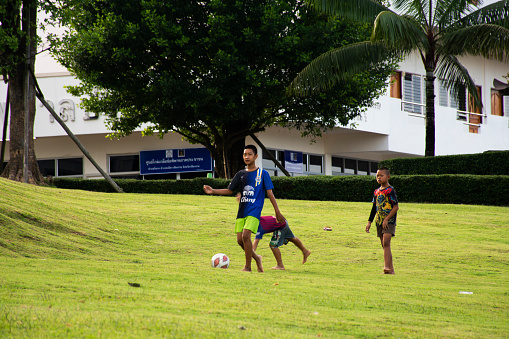 Asian children or thai kid and friends run playing football or soccer or futsal on playground of grass yard in public garden park at Wat Huay Pla Kang temple on June 30, 2022 in Chiang Rai, Thailand