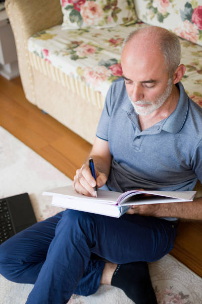 istock Handsome man sitting on carpet at home with books and doing homework 1412683074