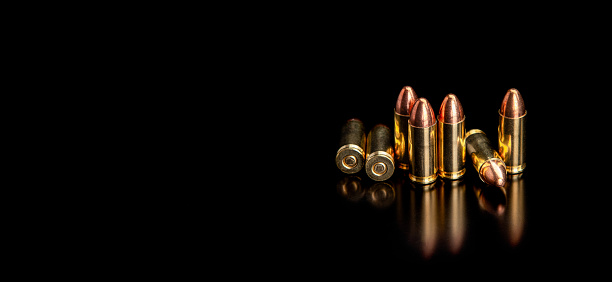 Pistol cartridges 9 mm on a smooth glossy surface with reflections. Ammunition for pistols and PCC carbines on a dark background.