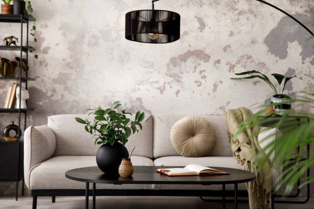 Loft style of modern apartment with design grey sofa, black coffee table, lamp and elegant personal accessories. Loft and industrial interior. Template.