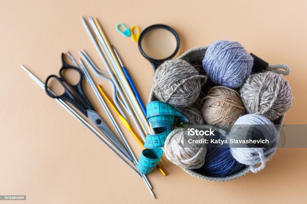 Knitting accessories Knitting accessories, hook, needles, scissors, magnifying glass, centimeter, a basket with blue gray brown balls of thread on an orange background. Knitting Needle Stock Photo