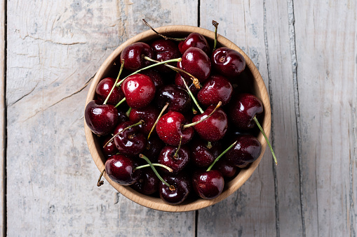 Fresh cherries with water drops in wooden bowl on white wooden table