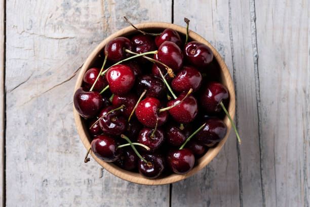 Fresh cherries with water drops Fresh cherries with water drops in wooden bowl on white wooden table cherry stock pictures, royalty-free photos & images