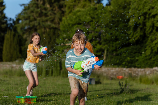 A father and his young son and daughter having a great time playing on the grass in a field in the North East of England. They are enjoying quality time together during a water gun fight.
