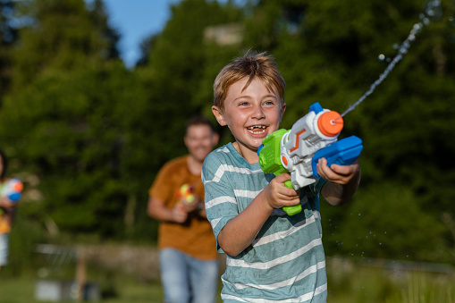 A young boy having a great time playing on the grass in a field in the North East of England. He is enjoying a water gun fight.