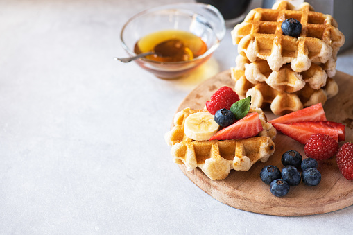 Waffles with berries and honey and coffee on a wooden board. Close up and copy space. Breakfast or brunch concept.