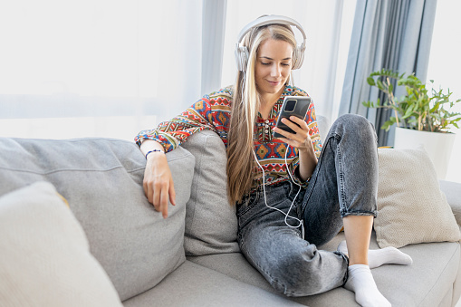 Young cheerful woman smiling and using mobile phone and headphones in the process of learning second language