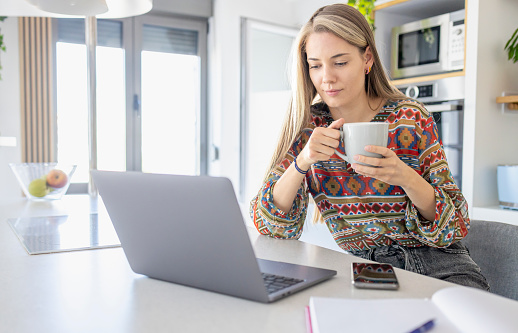 Young woman sipping coffee when looking at laptop