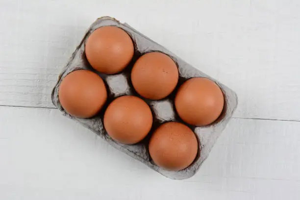 High angle shot of a six pack of organic brown eggs on a rustic white wood table. Horizontal format with copy space.
