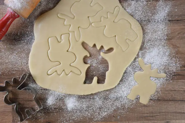 Cookie dough with moose shapes cutter and rolling pin on a floured wood kitchen table. Christmas Baking theme.