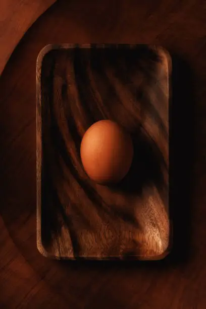 Flat lay still life of a single brown egg on a wooden tray on a round wooden platter.