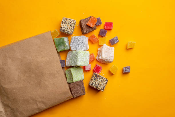 Turkish delight of different colors and shapes scattered on a yellow background from a paper bag. Organic  lokum stock photo