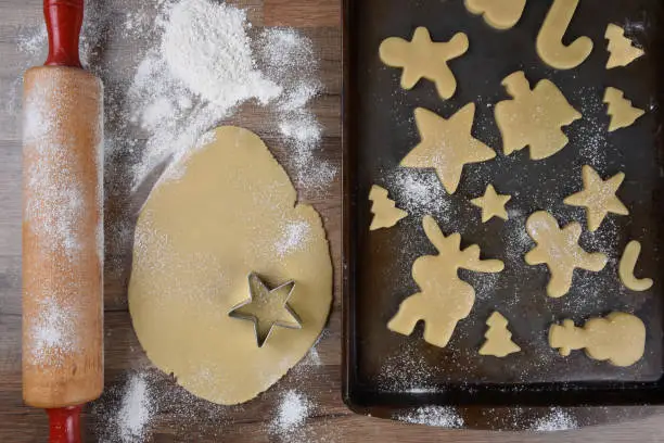 Top view of a baking sheet with a holiday shaped sugar cookies, with raw dough and rolling pin on the side.