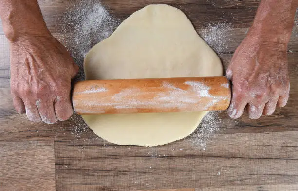 Rolling out Cookie Dough:  Close up of male hands using a rolling pin to prepare dough for making cookies on a wood kitchen table.