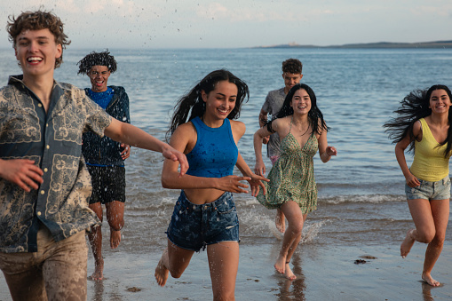 Group of mixed age and ethnicity teenage friends racing while on a beach in Beadnell, North East England. They are laughing, having fun by the ocean.