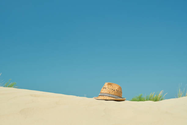Straw hat on the sand on the beach against the blue summer sky, close-up, copy space for text. A beautiful sunny day. Vacation, summer concept stock photo