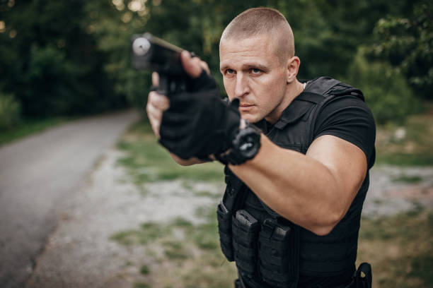 Portrait of a SWAT team soldier standing outdoors and aiming with a handgun.