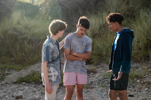 Group of teenage male friends at the beach in Beadnell, North East England. They are talking and comforting one of their friends who looks upset.