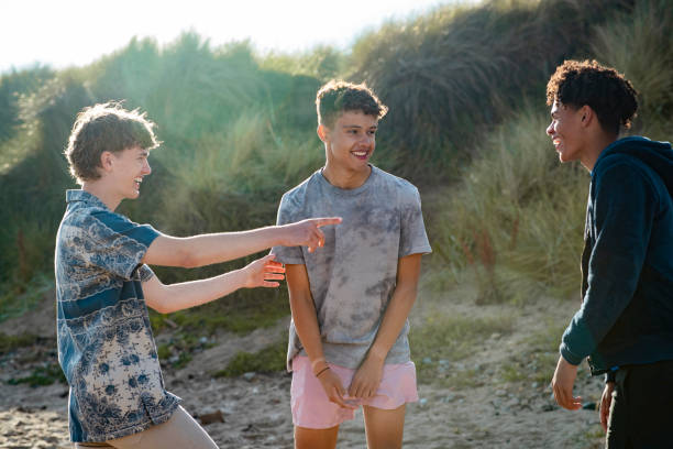 Group of teenage male friends relaxing at the beach in Beadnell, North East England. They are talking and laughing together.