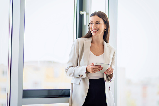 Portrait of attractive businesswoman using digital tablet while standing at window in a modern office.