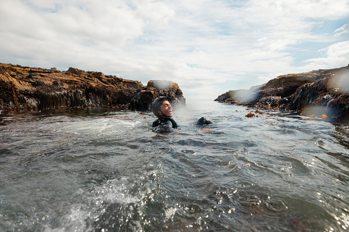 Teenage boy swimming in the ocean in the North East of England at Beadnell. He is wearing a wet suit and life jacket, laughing while he explores between the rocks.