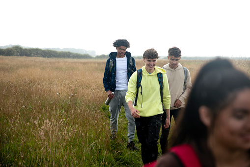 Group of mixed age and ethnicity teenage friends on a walk in Beadnell, North East England. They are walking through a field together in the rain.
