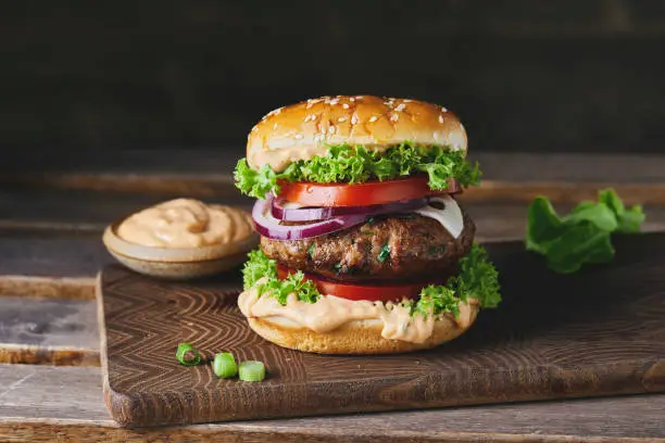 Beautiful, colorful and tasty hamburger on a homemade wooden cutting board and dark background, with a large copy space area