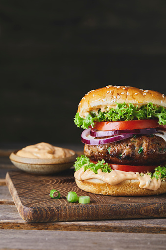 Colorful and tasty burger on a homemade wooden cutting board and dark background