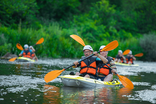 Senior male kayakers are kayaking in pairs together while going all together as a group